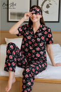 Woman wearing a black floral pajama set and a matching eye mask, sitting on a bed.