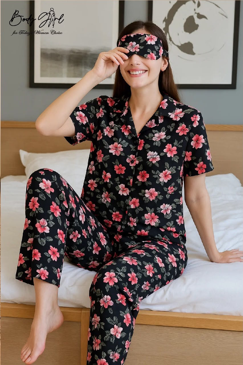 Woman wearing a black floral pajama set and a matching eye mask, sitting on a bed.