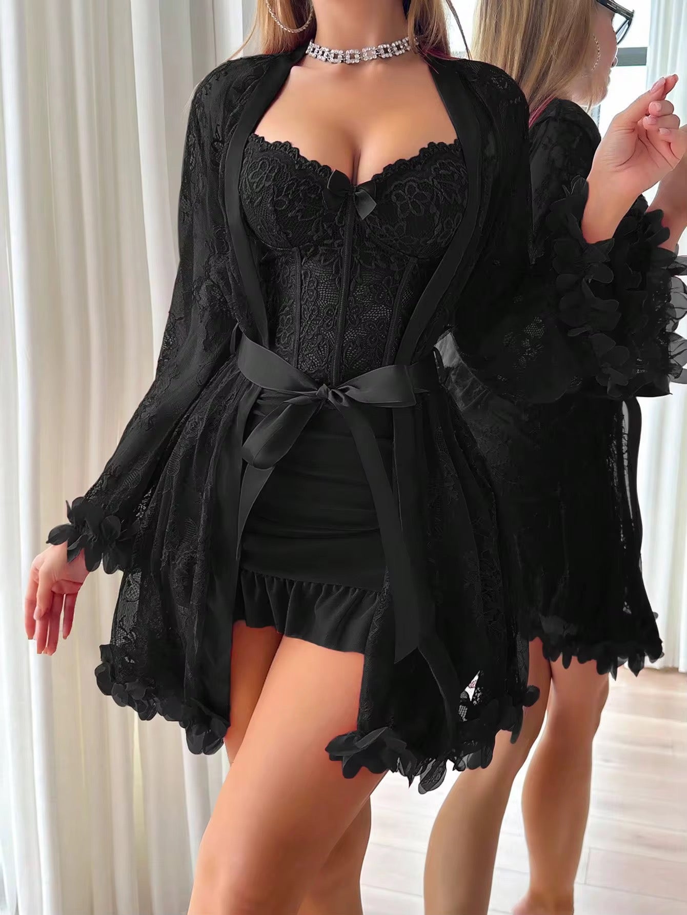 Person wearing a black lace outfit with a matching robe in a neutral setting.
