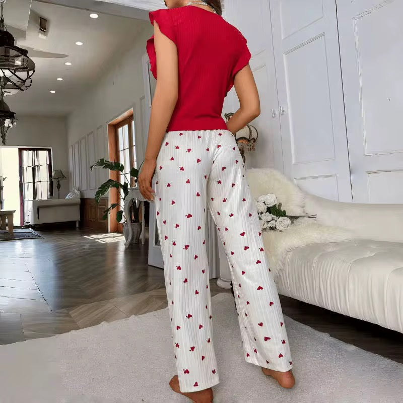 Person wearing a red top and white pants with red heart patterns in a living room.