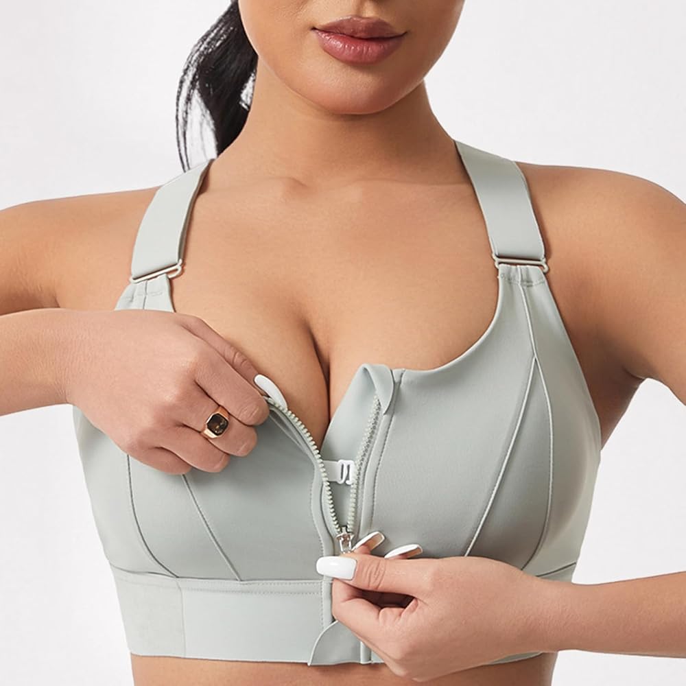 A close-up of a woman wearing a sage green wireless bra with a front zipper, demonstrating how to open it. The background is a clean, neutral white studio setting.