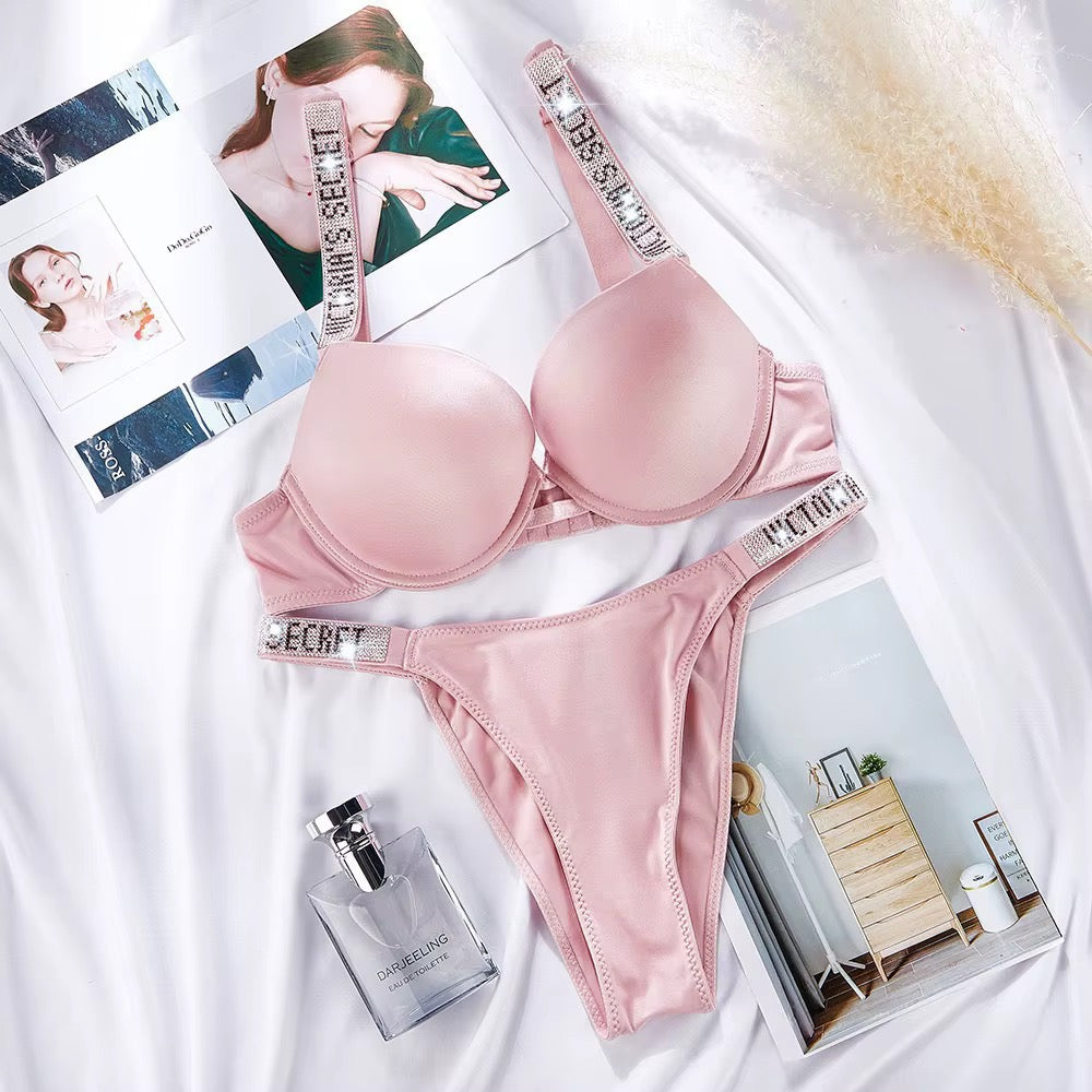 Pink lingerie set with 'Secret' branding on a white surface, surrounded by magazines and a perfume bottle.