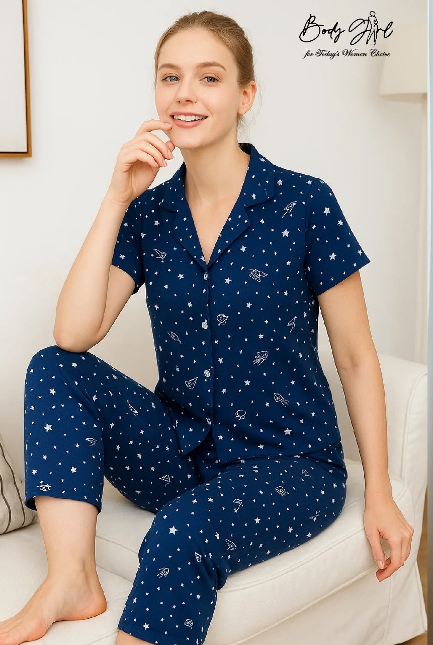 Woman wearing a navy blue pajama set with celestial pattern on a white couch.