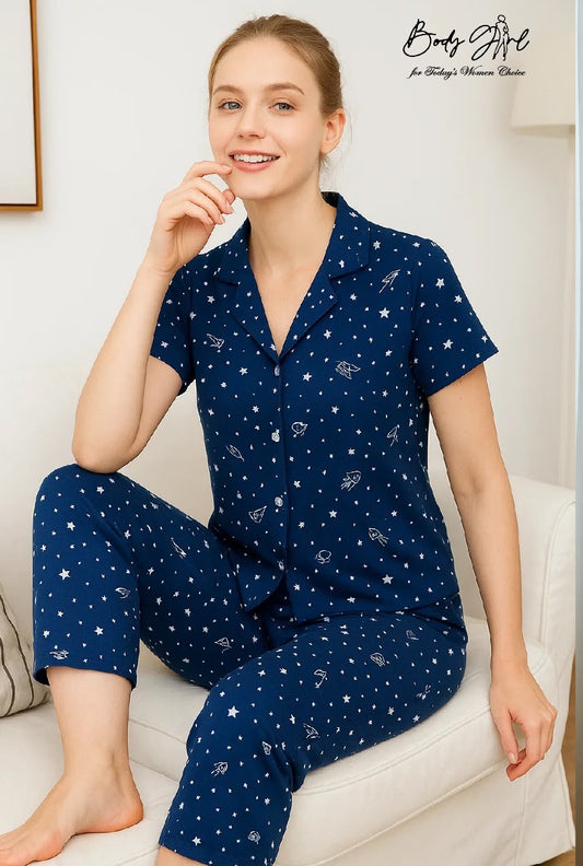 Woman wearing a navy blue pajama set with celestial pattern on a white couch.